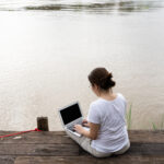 asian adult woman using computer to work remotely from riverside