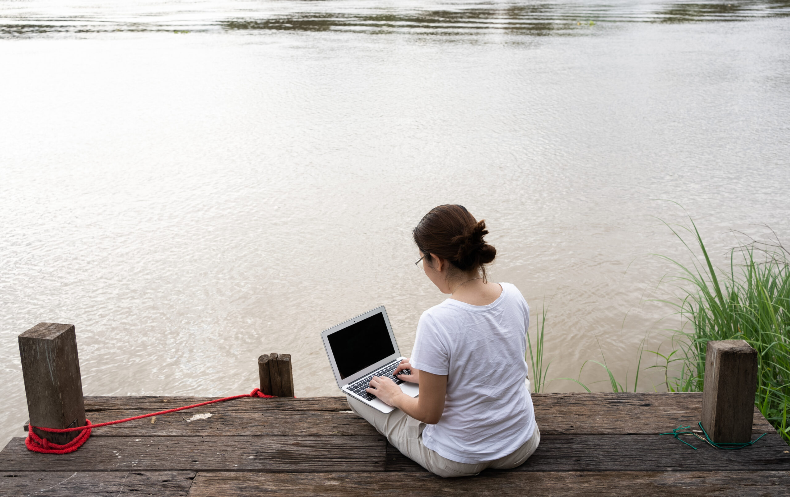 asian adult woman using computer to work remotely from riverside