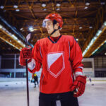 Attractive strong hockey player standing on the ice in hall and holding a stick.