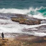 beautiful-shot-person-s-silhouette-standing-rock-near-beach-looking-waves_11zon